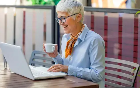 older lady outside on a patio drinking tea and scrolling grindr on a laptop